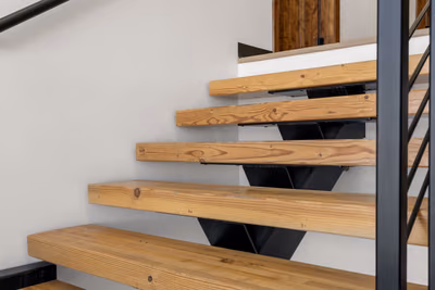 Close view of solid timber stair treads on black steel brackets beside a black steel post, with a wooden door at the top of the stair.